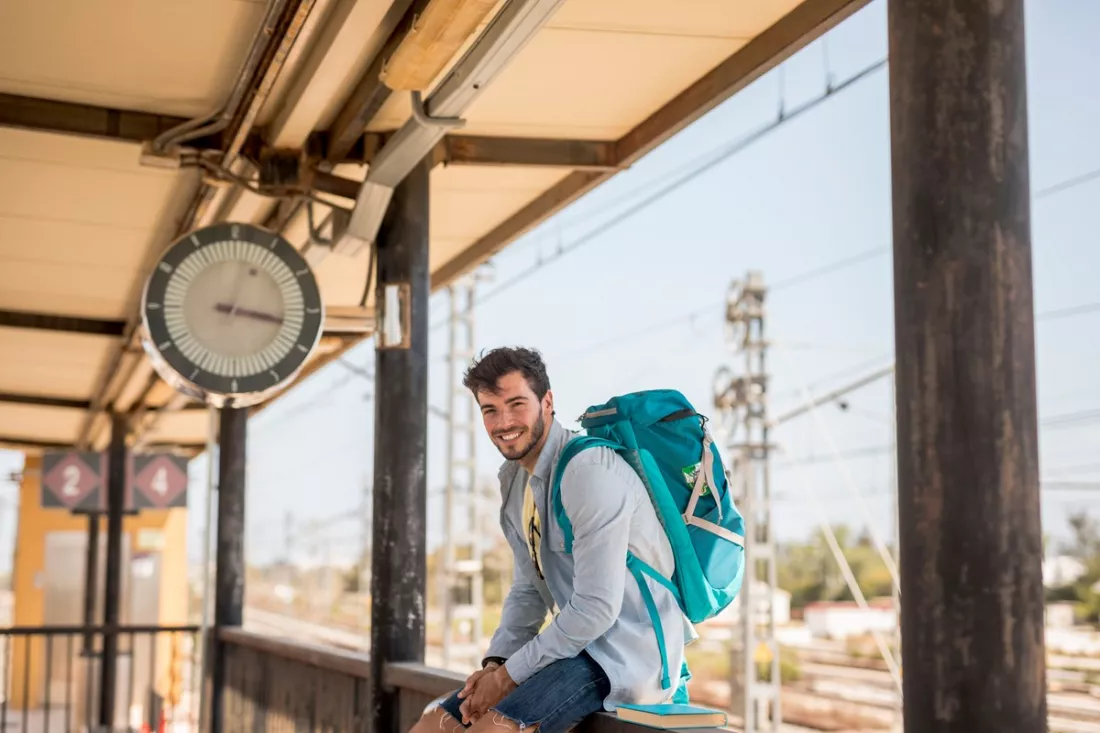 A smiling traveller waiting for a train under a station clock